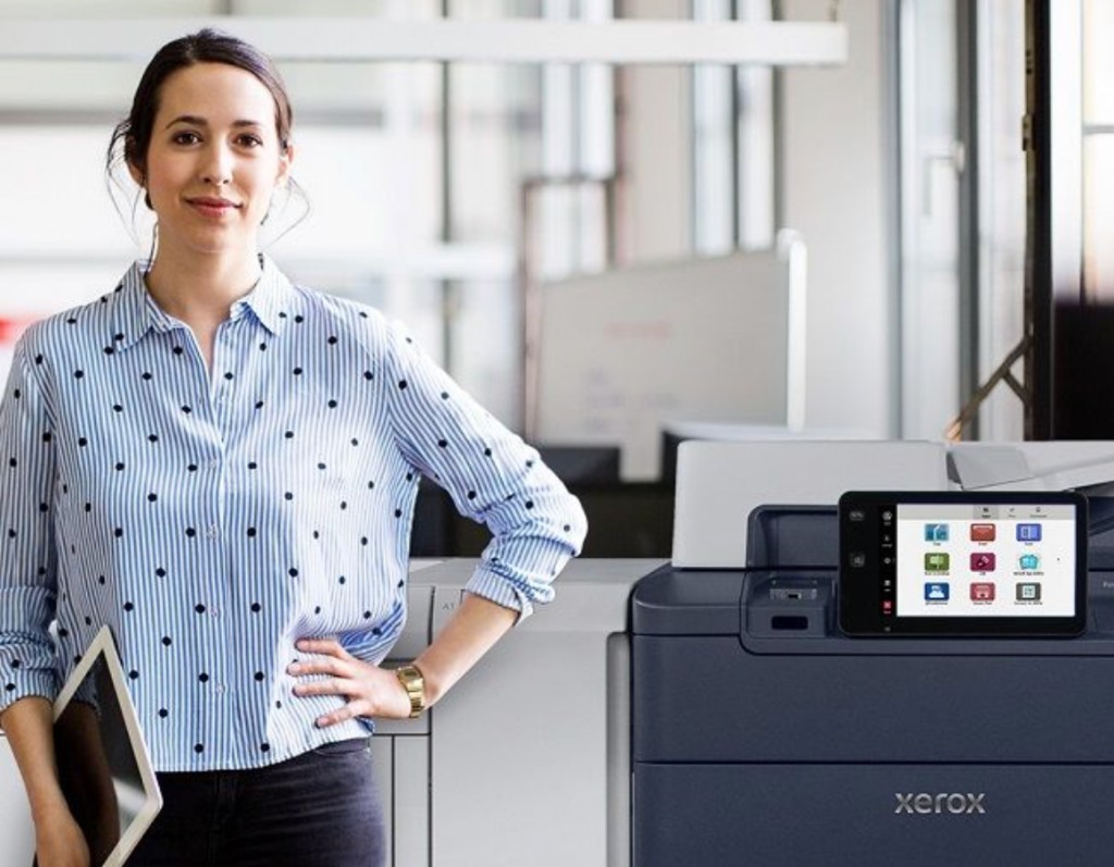 Office team member standing beside a Xerox® PrimeLink® C9275 production printer in a modern workspace