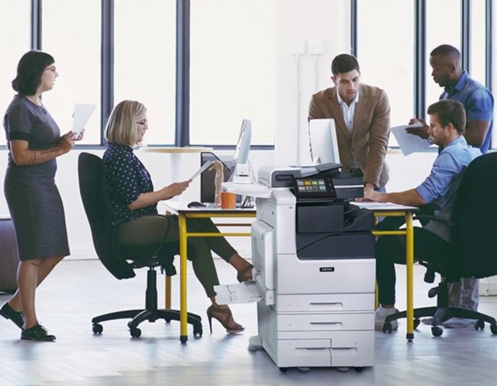 Office team working around a Xerox® VersaLink® C7130 multifunction printer in a modern workspace